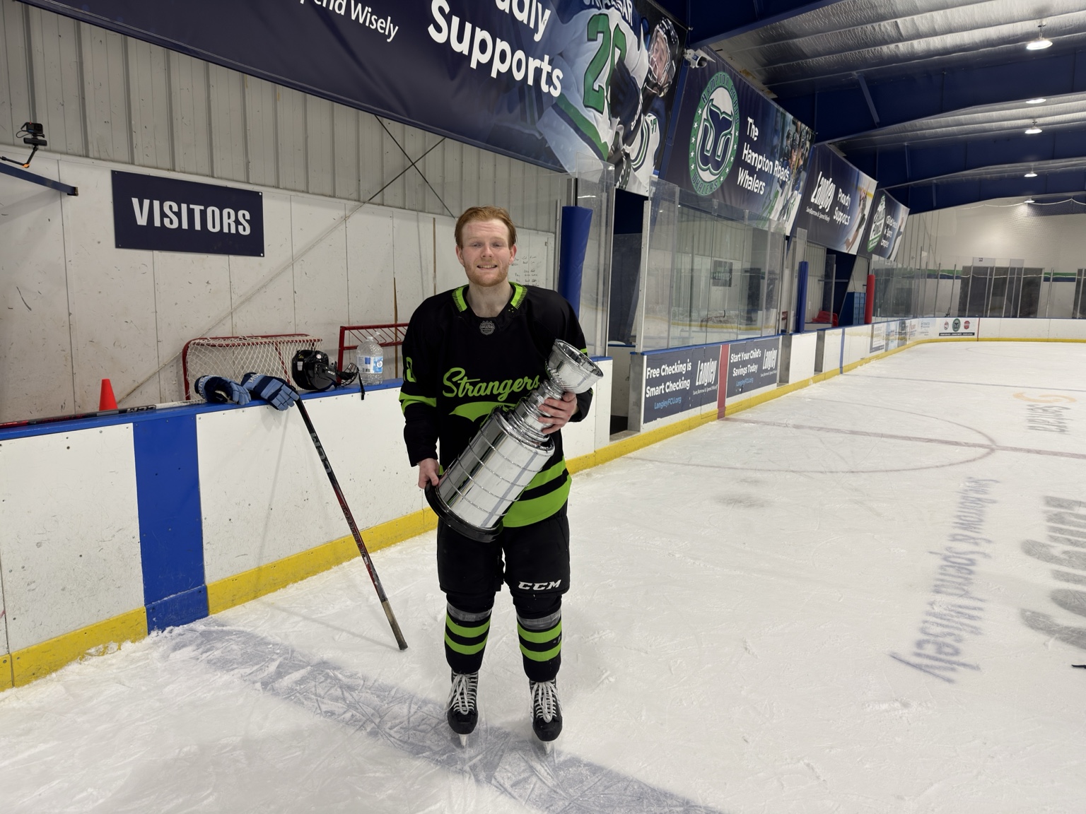 A Strangers player stands on the ice holding the championship trophy.