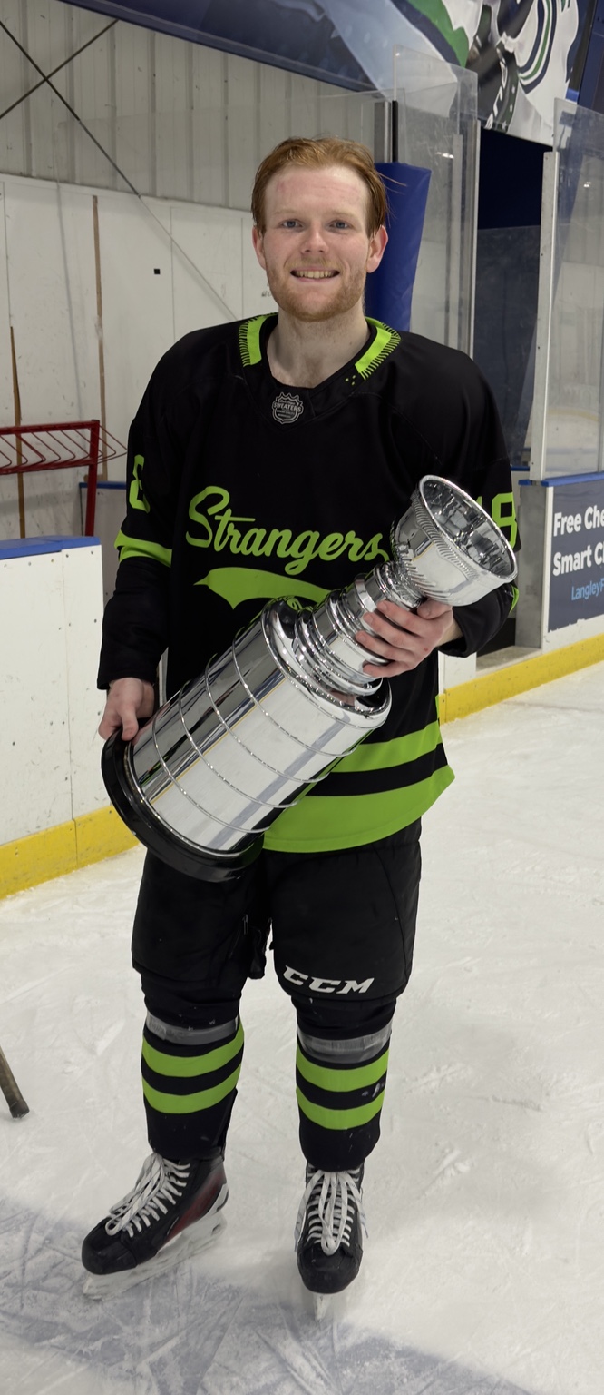 A Strangers player poses on the ice with the championship trophy.