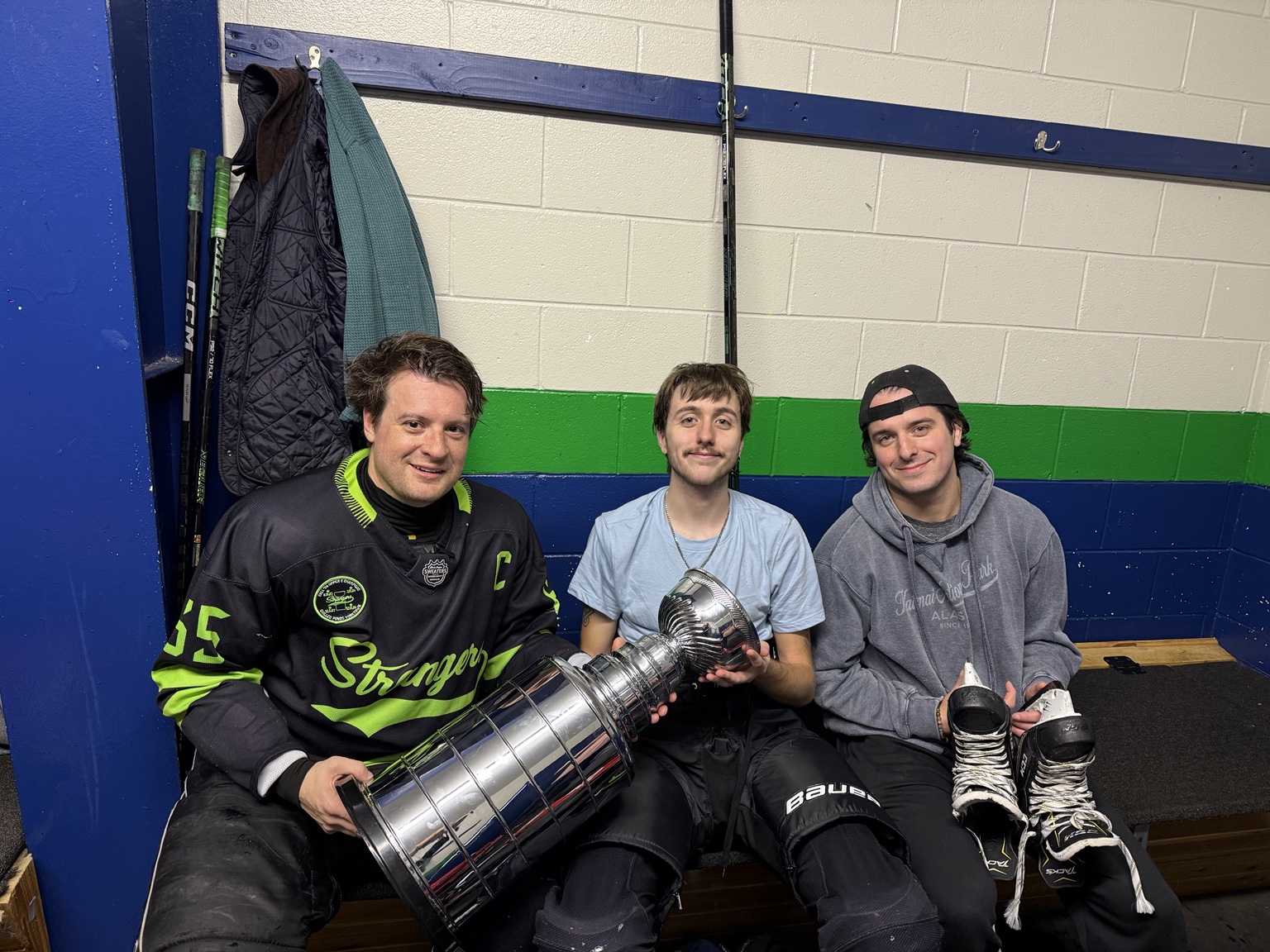 Three Strangers teammates sit with the championship trophy in the locker room.