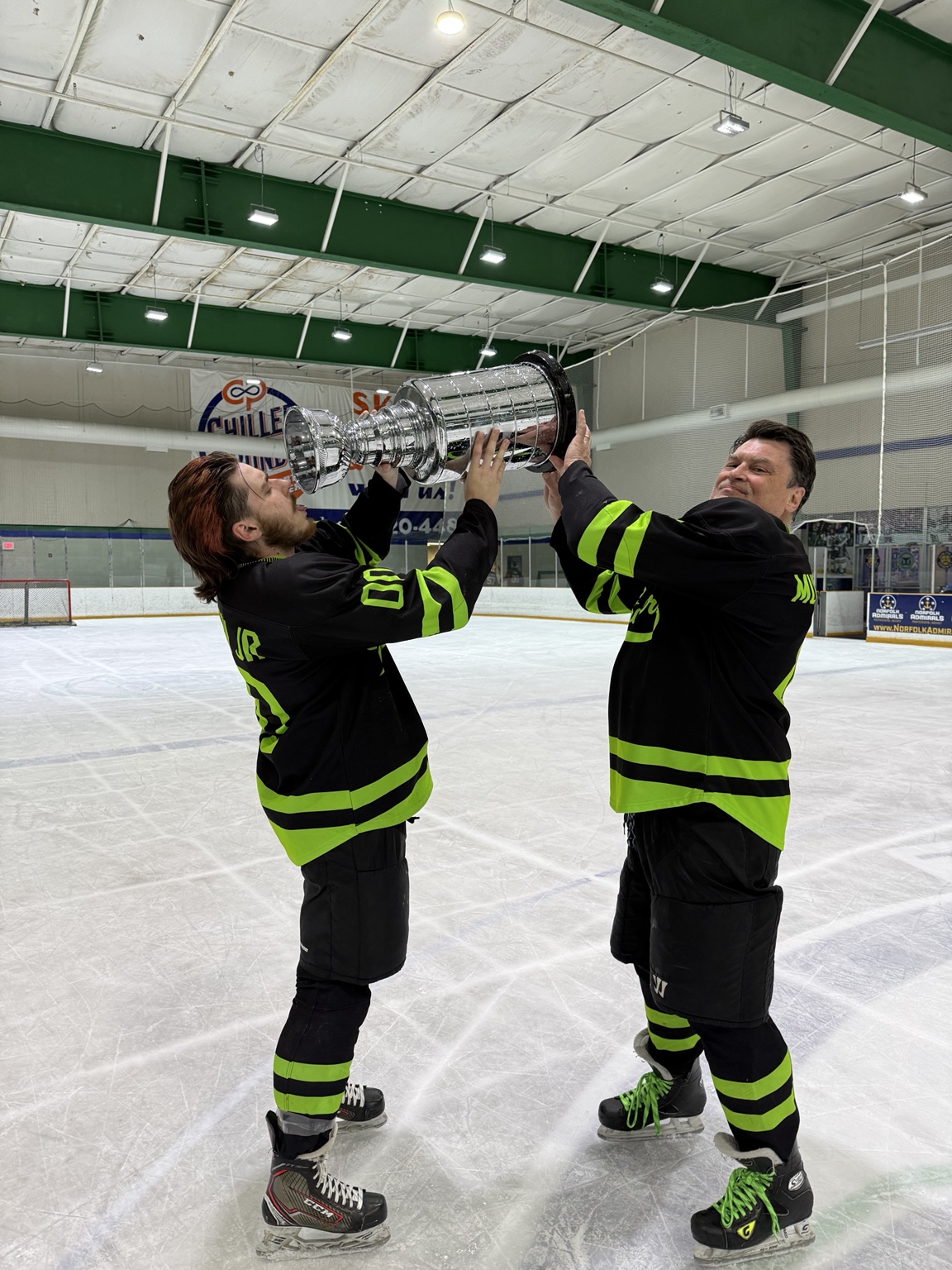 Two Strangers teammates lift the trophy together on the ice.