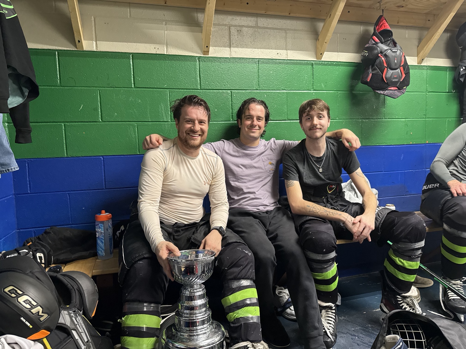 Three Strangers teammates sit together with the championship trophy in the locker room.